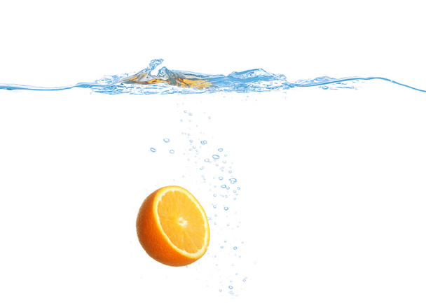 Ripe orange falling down into clear water against white background - 写真・画像