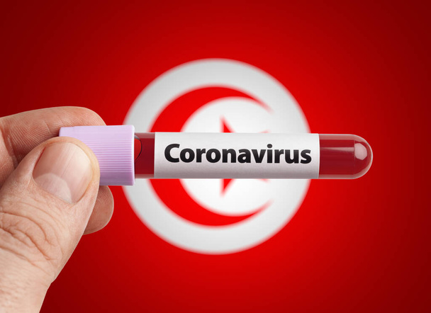 チュニジアの旗の前の試験管でコロナウイルスに感染した血液を保持する科学者。世界の概念の国々でのパンデミックコヴィト19感染. - 写真・画像