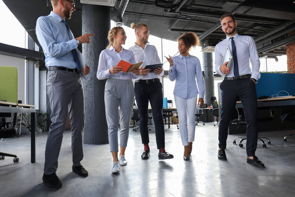 Σύγχρονοι επιχειρηματίες συζητούν για δουλειές και χαμογελούν ενώ περπατούν στο διάδρομο του γραφείου - Φωτογραφία, εικόνα