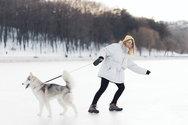 Onnellinen nuori tyttö leikkii siperialaisen husky koiran kanssa talvipuistossa. He kävelevät jäätyneellä järvellä
 - Valokuva, kuva