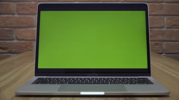 オフィスの机の上に緑の画面を持つノートパソコン。ドリーズーム撮影。ロフトスタイルのオフィス。背景にレンガの壁があります. - 映像、動画