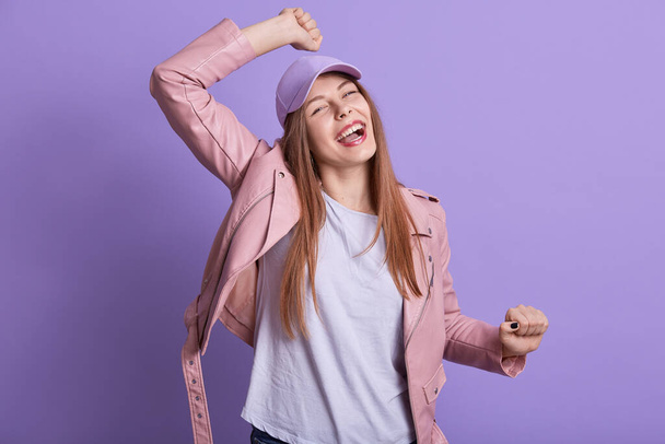 Picture of emotional cheerful energetic young female raising her arms, dancing, having fun, spending free time alone, being in high spirits, wearing casual clothes. People and emotions concept. - Photo, Image