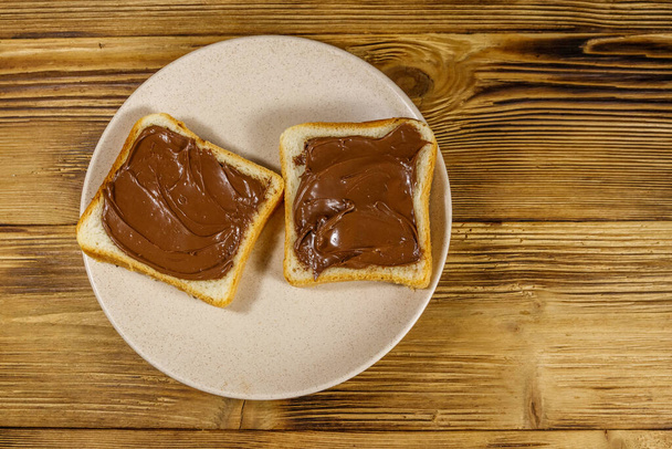 Two slices of bread with delicious chocolate hazelnut spread on wooden table. Top view - Foto, afbeelding