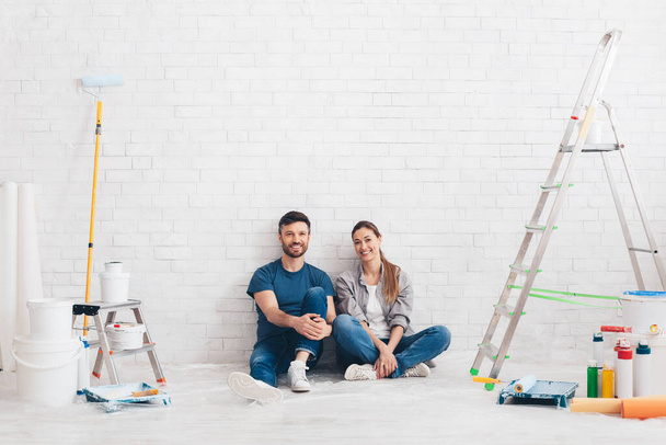 Młoda kochająca się para siedzi w nowym mieszkaniu z narzędziami do malowania - Zdjęcie, obraz