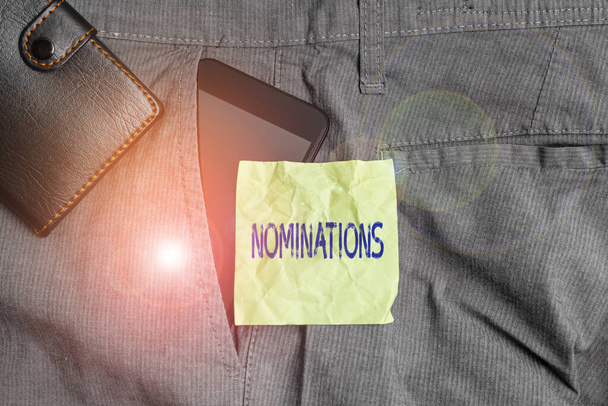 Handwriting text writing Nominations. Concept meaning action of nominating or state being nominated for prize Smartphone device inside trousers front pocket with wallet and note paper. - Photo, Image