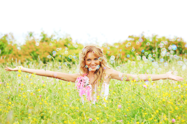 Chica rubia comienza burbujas de jabón y sonriendo en un campo de primavera verde
 - Foto, Imagen