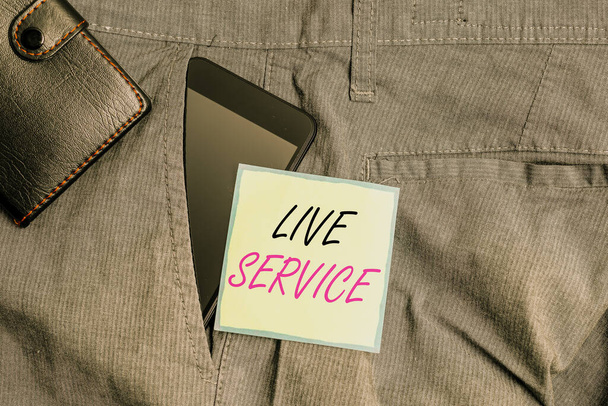 Text sign showing Live Service. Conceptual photo Extending or providing help to others in verbal or action way Smartphone device inside trousers front pocket with wallet and note paper. - 写真・画像
