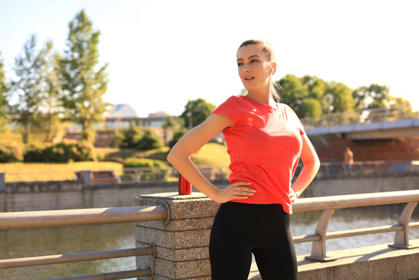 Mulher bonita em roupas esportivas sorrindo e olhando uma câmera enquanto se exercita ao ar livre
 - Foto, Imagem