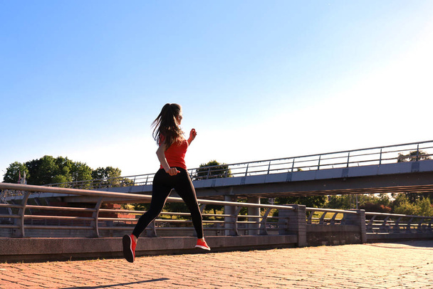 Photo of modern young woman in sports clothing jumping while exercising outdoors - Foto, Imagem