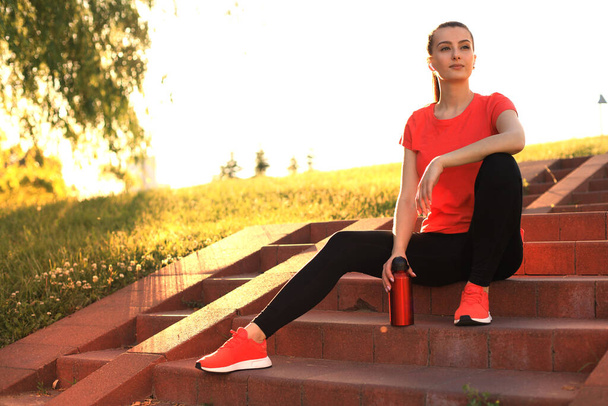 Attractive young woman in sports clothing resting while sitting on the stair with evening sunlight - Foto, Bild