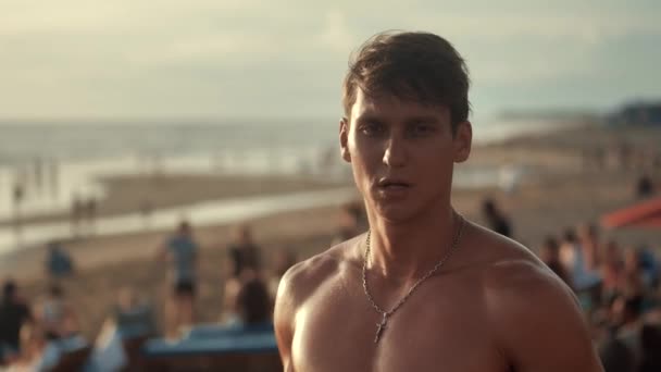 Retrato de un hombre musculoso guapo con un torso desnudo en la playa al atardecer
. - Metraje, vídeo
