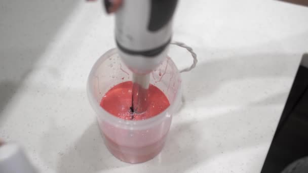 Las manos femeninas mezclan líquido rosa con pintura roja, cilindro de plástico, licuadora, primer plano
. - Imágenes, Vídeo