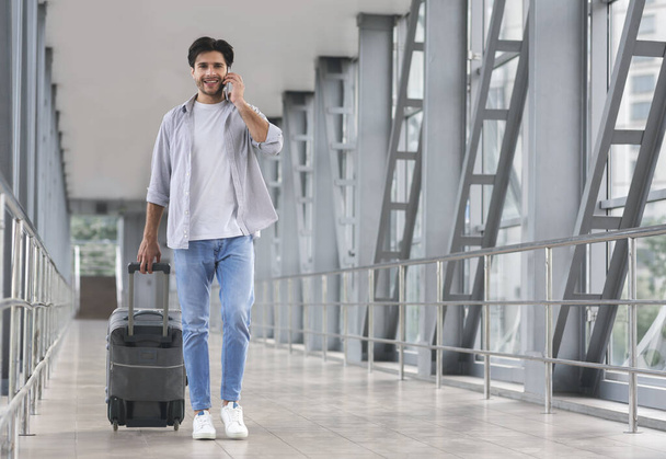 Homem viajante andando com bagagem no aeroporto e falando no celular
 - Foto, Imagem