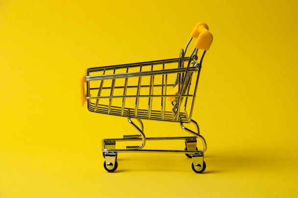 Winkelwagen voor winkelen op gele achtergrond. Supermarkt voedselprijs concept, vakantie kortingen - Foto, afbeelding