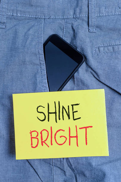 Tekst do pisania słów Shine Bright. Koncepcja biznesowa dla podjęcia wysiłku, aby żyć normalnie, gdy w trudnej sytuacji Smartphone urządzenie wewnątrz formalnej kieszeni spodni roboczych przedniej kieszeni w pobliżu papieru notatkowego. - Zdjęcie, obraz
