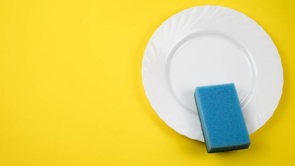 esponja de limpieza azul sobre placa blanca sobre fondo amarillo con espacio de copia
. - Foto, Imagen