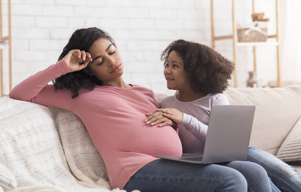 Donna incinta stanca con figlioletta che lavora sul computer portatile a casa
 - Foto, immagini