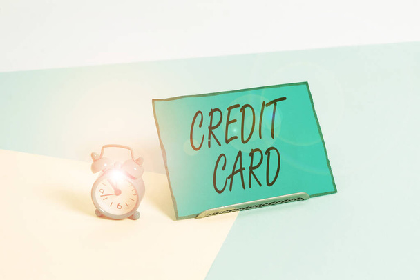 Conceptual hand writing showing Credit Card. Business photo showcasing card that allows you to borrow money against a line of credit Alarm clock beside a Paper sheet placed on pastel backdrop. - Foto, Bild
