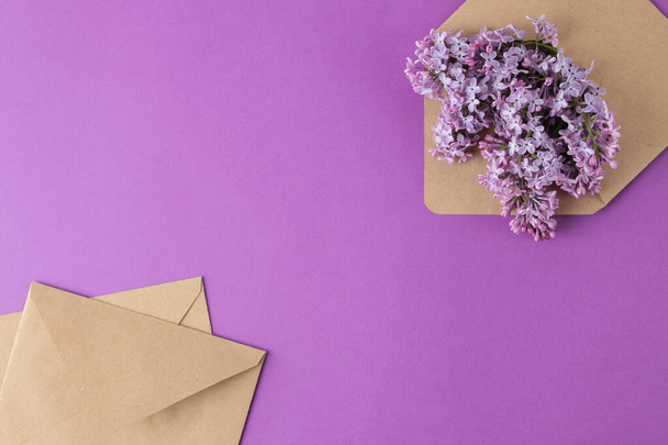 Весняні квіти. квітучі бузкові квіти в ремісничому конверті на яскраво-фіолетовому тлі. вид зверху
 - Фото, зображення