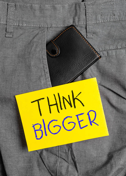Writing note showing Think Bigger. Business photo showcasing being able to dream and visualise what you can achieve Small wallet inside trouser front pocket near notation paper. - Foto, afbeelding
