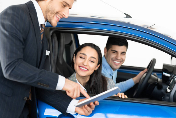 Happy Couple Buying Car Talking With Dealer Sitting In Auto - 写真・画像