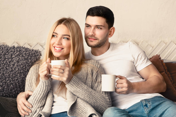 Newlyweds with hot tea cuddling on sofa indoors - Fotó, kép