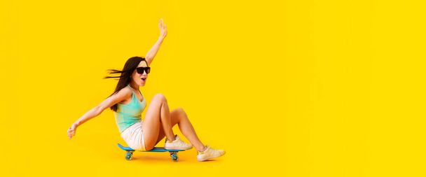 美しいサングラスの少女、スケートボードに座って、黄色の背景に画像、コンセプト正夏気分、テキストのためのスペースとパノラマモックアップ - 写真・画像