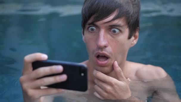 Испуганный человек неприятно шокирован тем, что увидел на своем смартфоне, расслабляясь в бассейне
. - Кадры, видео