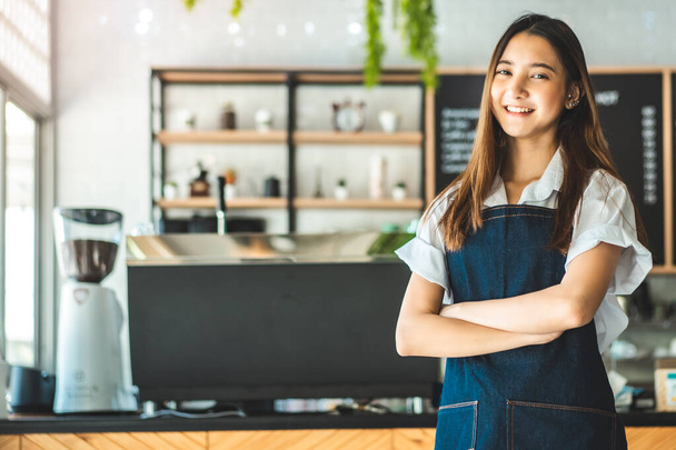 Pretty young asian waitress standing arms crossed in cafeteria.Coffee Business owner Concept.  barista in apron smiling at camera in coffee shop counter - Valokuva, kuva