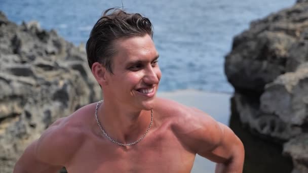 jong mannelijk model poseren in de zomer middag op het strand op een achtergrond van de zee - Video