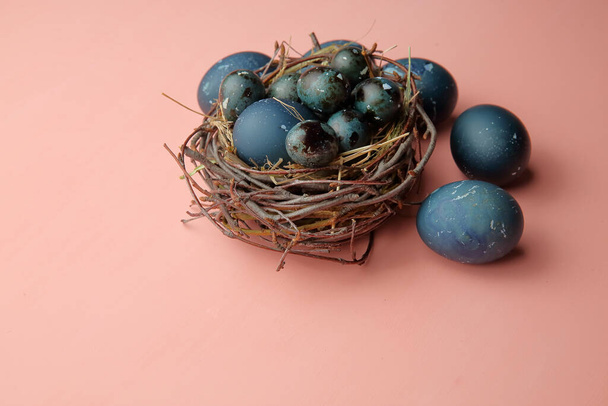 Huevos pintados con una piedra azul yacen en un nido sobre un fondo rosa, Pascua
. - Foto, imagen