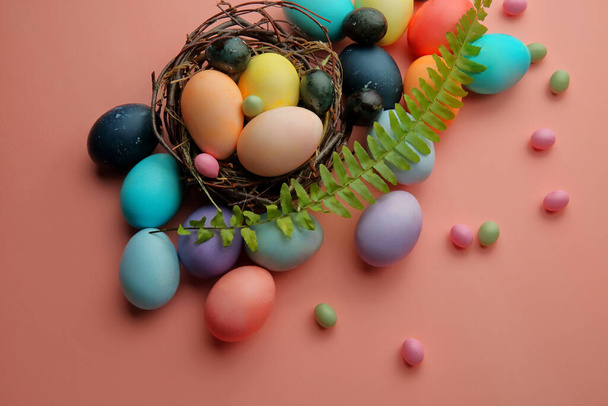 Многоцветные яйца и леденцы в гнезде на розовом фоне с веточкой папоротника, Пасха
. - Фото, изображение