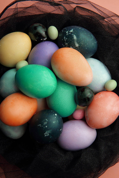 Huevos multicolores y piruletas en un nido de tela negra sobre un fondo rosa, Pascua
. - Foto, imagen
