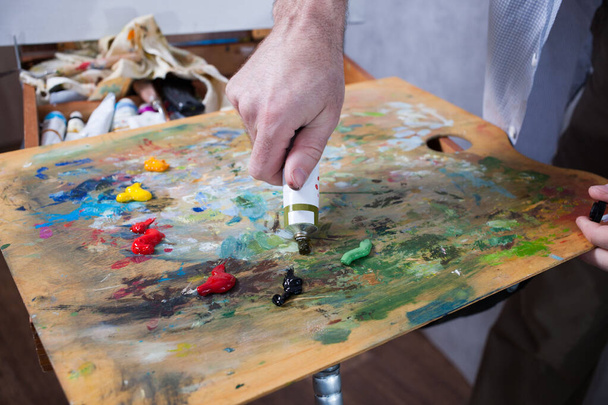 Ο καλλιτέχνης συμπιέζει το χρώμα από ένα σωλήνα σε μια παλέτα. Κοντινό πλάνο - Φωτογραφία, εικόνα