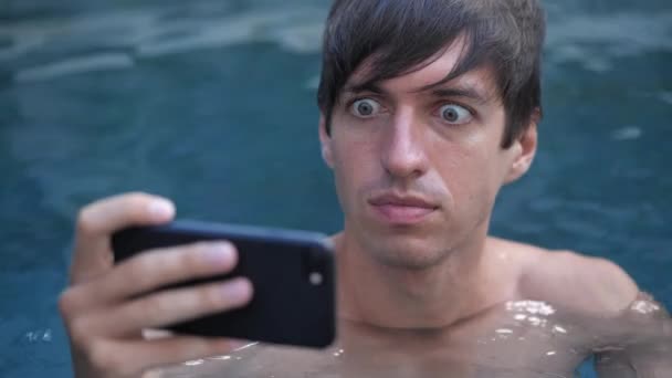 Przerażony człowiek jest nieprzyjemnie zszokowany tym, co zobaczył na swoim smartfonie, relaksując się w basenie.. - Materiał filmowy, wideo