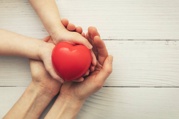rood hart in kinder- en moederhanden op witte houten ondergrond. concept van liefde, liefdadigheid, empathie - Foto, afbeelding