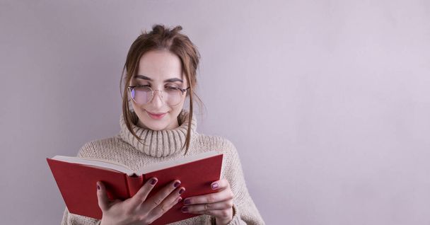 A young girl in glasses is reading a book. woman on a gray background. The concept of education and information. Free space for text.Banner. Long format - Foto, immagini