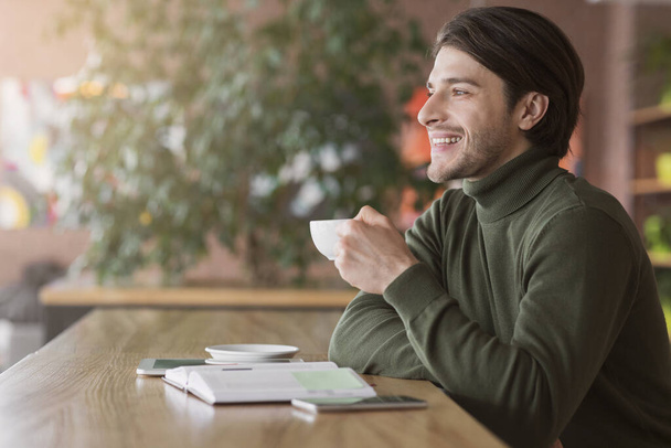 Geïnspireerde man die koffie drinkt in café, kijkend naar kopieerruimte - Foto, afbeelding