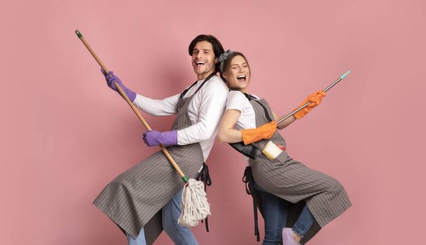 Cleaning Fun. Couple Fooling With Mop And Broom On Pink Background - 写真・画像