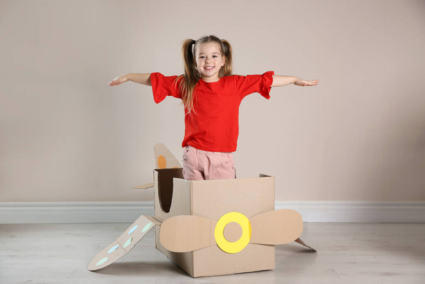 Cute little child playing with cardboard plane near beige wall - Фото, зображення