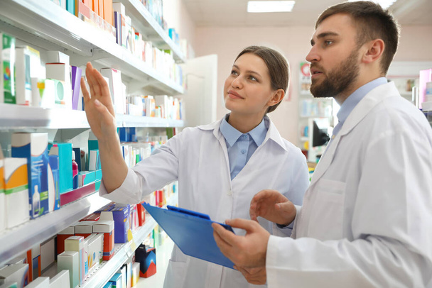 Professional pharmacists near shelves in modern drugstore - Foto, afbeelding