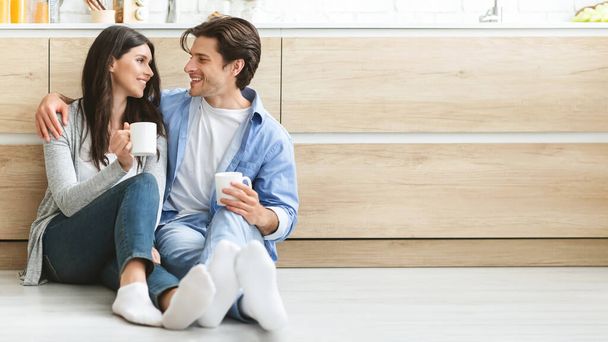 Jovem casal desfrutando de café, sentado no chão na cozinha
 - Foto, Imagem