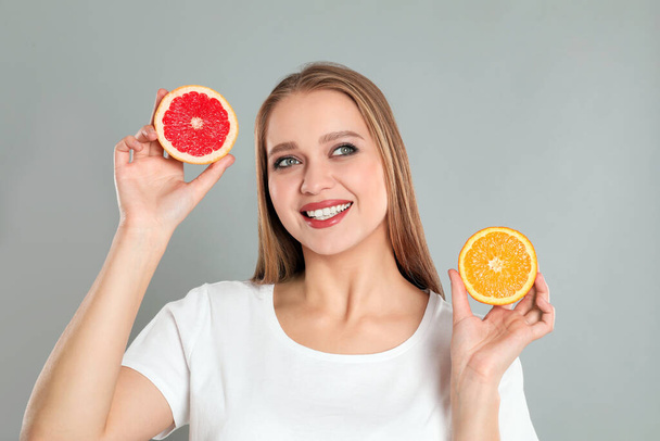 Young woman with cut orange and grapefruit on grey background. Vitamin rich food - Valokuva, kuva