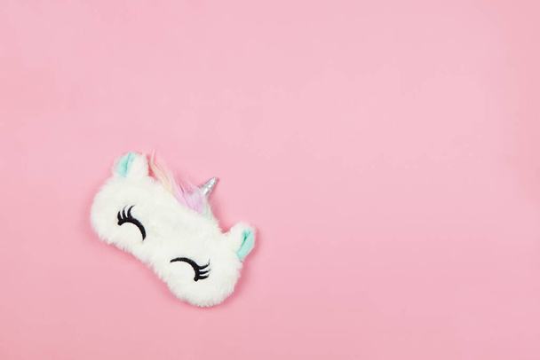White fluffy fur sleep mask unicorn with closed eyes and small ears on pastel pink paper background, copy space. Top view, flat lay. Concept of vivid dreams. Accessories for girls and young women - Photo, Image