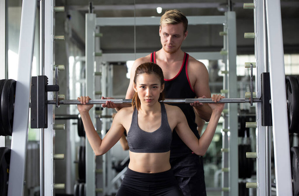 Προσωπικός γυμναστής που βοηθάει γυναίκες που δουλεύουν με βαρείς αλήτες στο γυμναστήριο. Γυμναστική γυμναστική γυναίκα στο γυμναστήριο προπόνηση αθλητισμού με αλτήρα και πρωτεΐνη κούνημα μπουκάλι υγιεινό τρόπο ζωής bodybuilding, αθλητής οικοδόμος μυς τρόπο ζωής. - Φωτογραφία, εικόνα