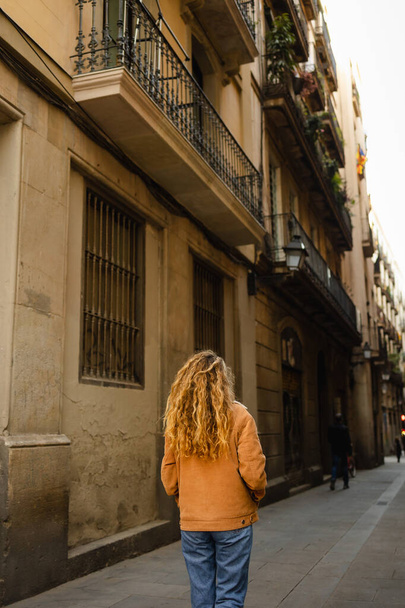 Girl walking through the streets in Barcelona. Cute girl with blond curly hair walking through the streets on Barcelona looking at the buildings and doing tourism. - Photo, image