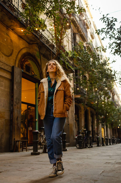 Dziewczyna spacerująca ulicami w Barcelonie. Cute girl z blond kręcone włosy spaceru ulicami na Barcelonie patrząc na budynki i robi turystykę. - Zdjęcie, obraz