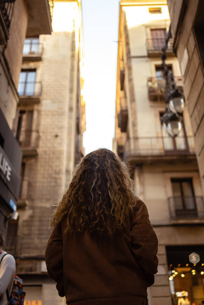 Girl walking through the streets in Barcelona. Cute girl with blond curly hair walking through the streets on Barcelona looking at the buildings and doing tourism. - Foto, Imagen