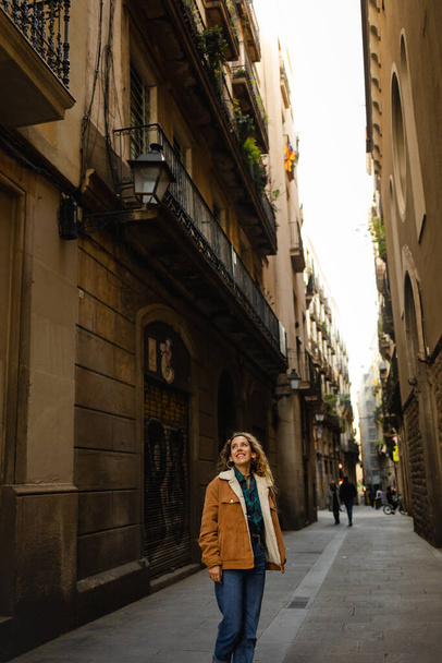 Barselona 'da sokaklarda yürüyen bir kız. Sarışın, kıvırcık saçlı, Barselona sokaklarında yürüyen binalara bakan ve turizm yapan tatlı bir kız.. - Fotoğraf, Görsel