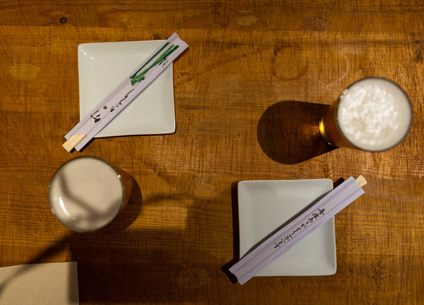 Καφέ τραπέζι με δύο μπύρες, δύο πιάτα και δύο σετ ξυλάκια. - Φωτογραφία, εικόνα
